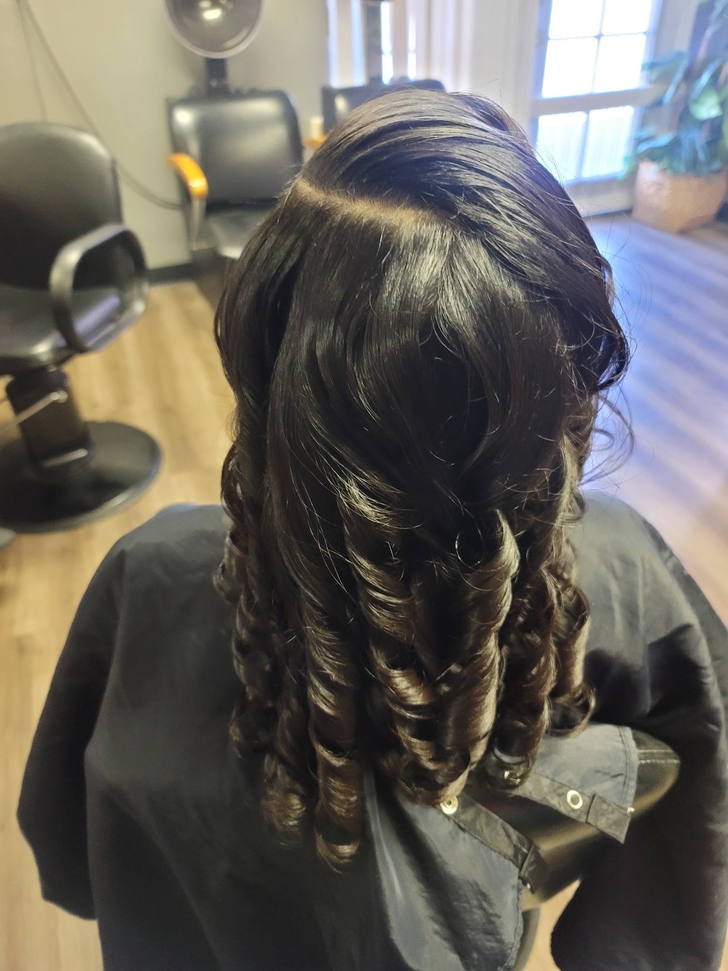 Dark, curled hair styled and draped over the back of a chair in a salon setting.