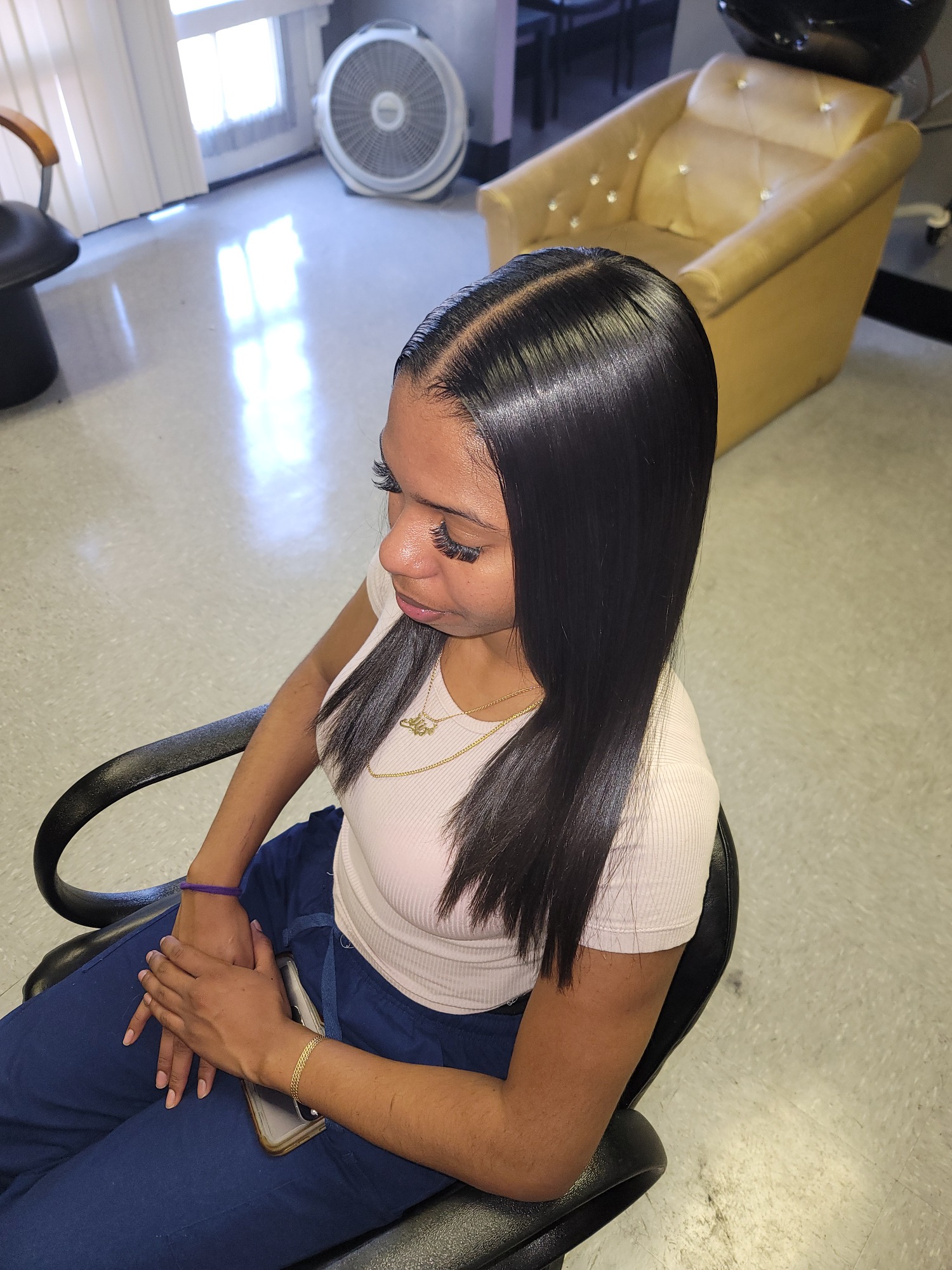 Young woman with straight, long hair sitting in a salon chair, hands clasped.