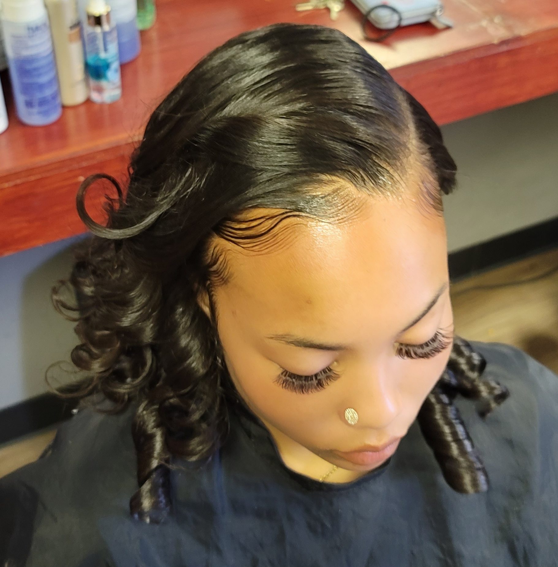 A close-up of a woman with styled, wavy hair and prominent eyelashes in a salon setting.