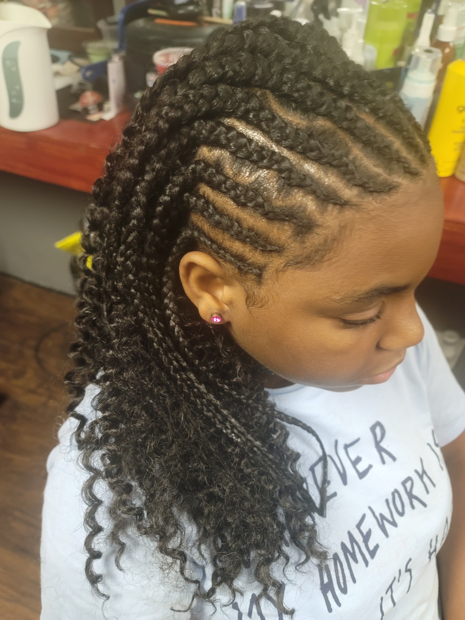 A young person with braided and curly hairstyle, featuring geometric patterns.