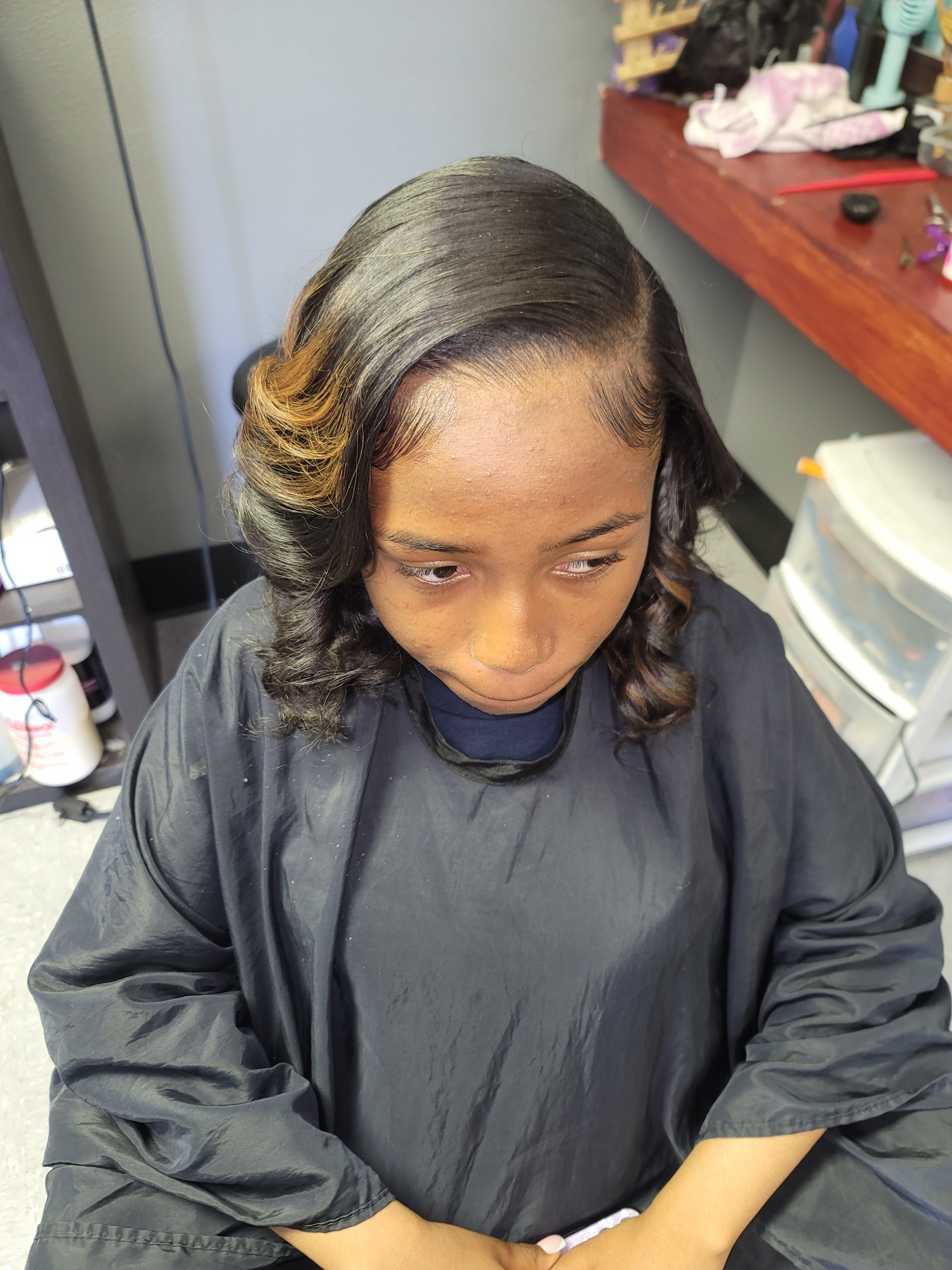 A young woman with styled hair wearing a black cape in a salon setting.