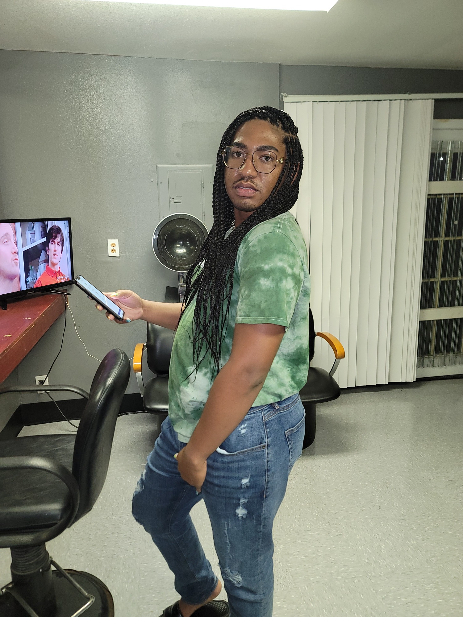 Person standing in a room, holding a phone and wearing a green tie-dye shirt.