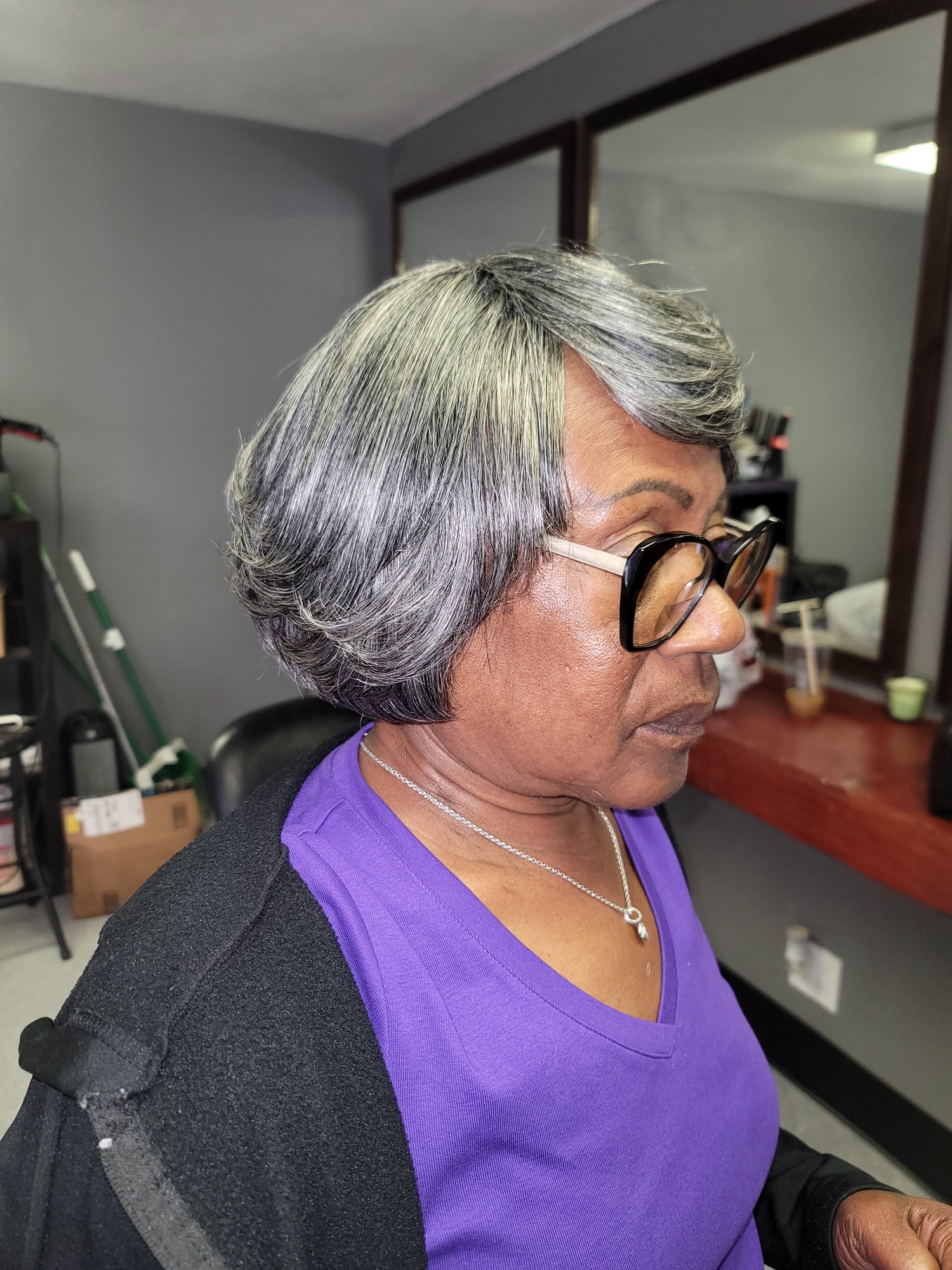 A woman with short gray hair and large glasses, wearing a purple top.
