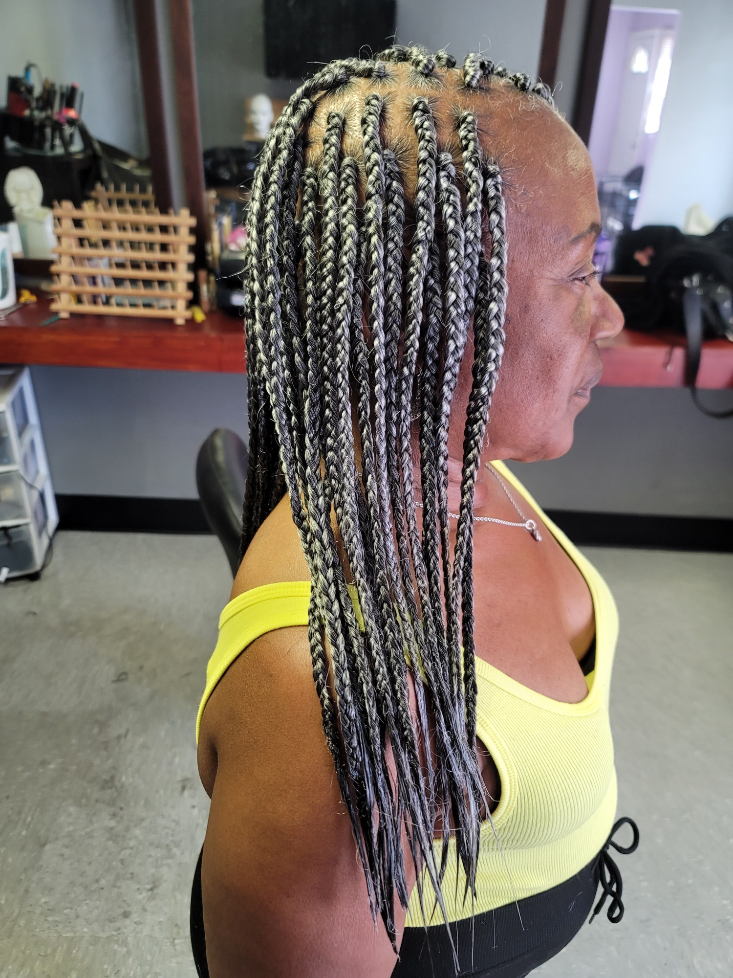 Woman with long, braided hair styled in a side profile, wearing a yellow top.