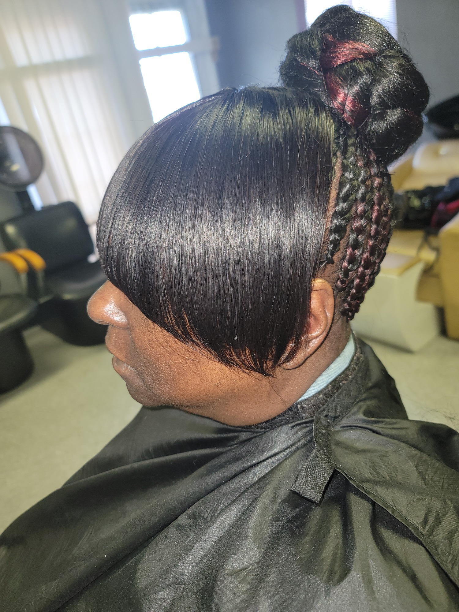 Close-up of a woman's hairstyle featuring a bun and long bangs with braided accents.