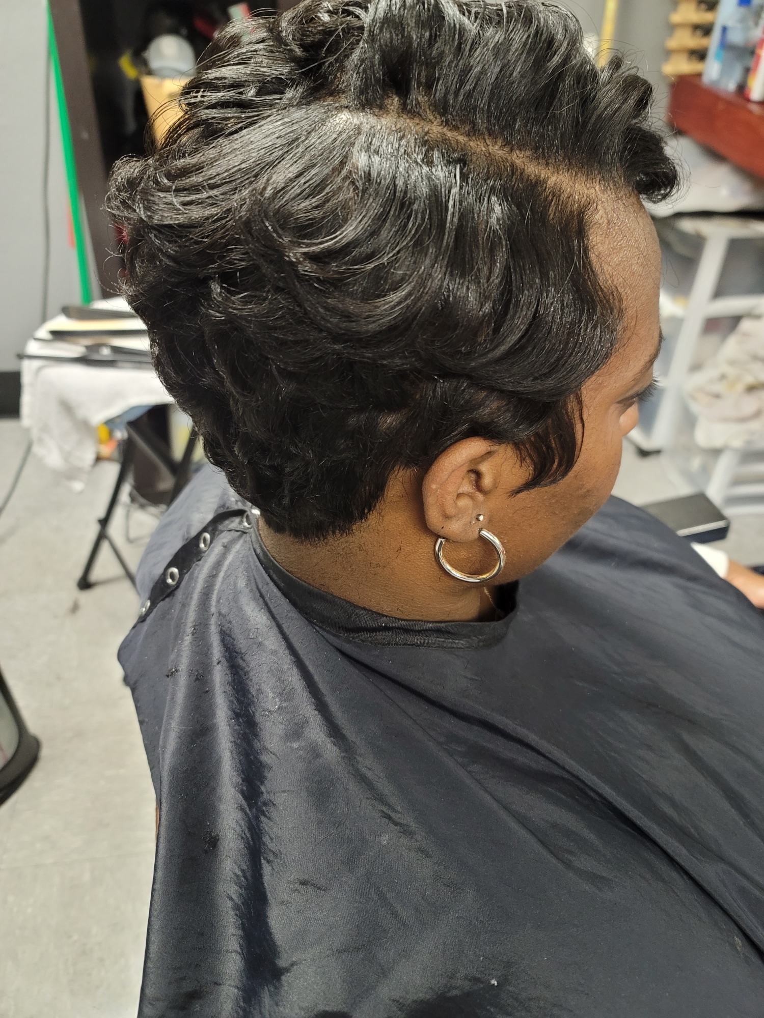 Short, stylish haircut on a person with dark hair, seated in a salon chair.